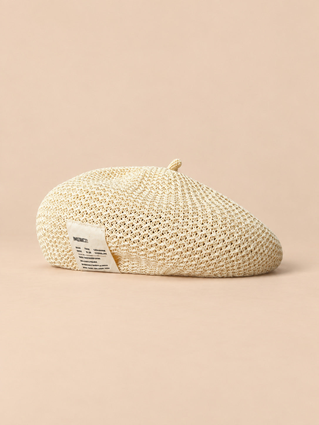 Béret d’été en lin ajouré beige, vue de face sur fond pêche sable
