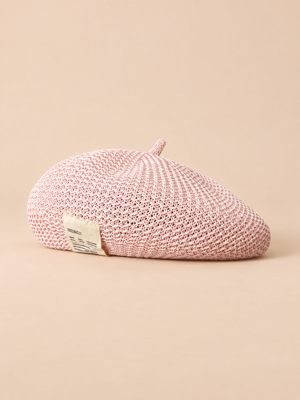 Béret d’été en lin ajouré rose, vue de trois quarts sur fond pêche sable