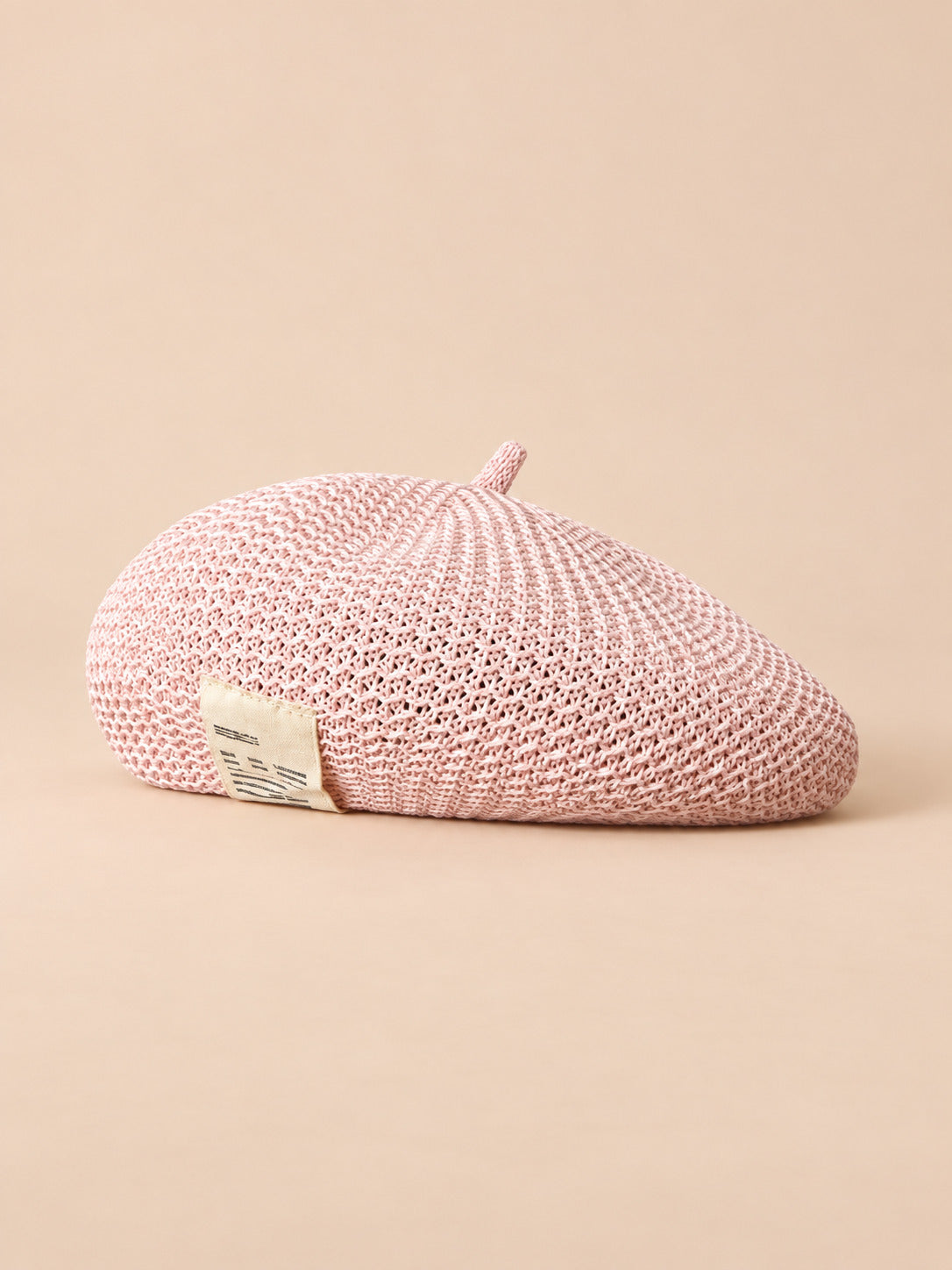 Béret d’été en lin ajouré rose, vue de trois quarts sur fond pêche sable