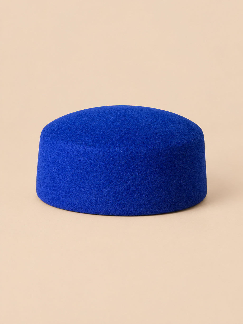 Béret femme en laine feutrée bleu, forme plat, vue de face sur fond pêche sable