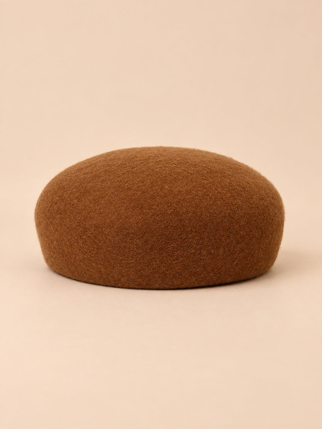 Béret femme en laine feutrée camel foncé, forme rond, vue de face sur fond pêche sable