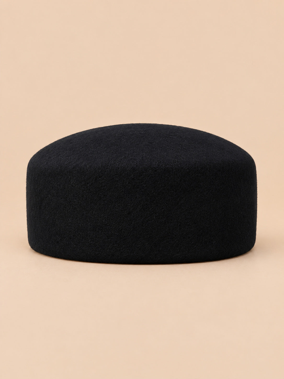 Béret femme en laine feutrée noir, forme dessus plat, vue de face sur fond pêche sable