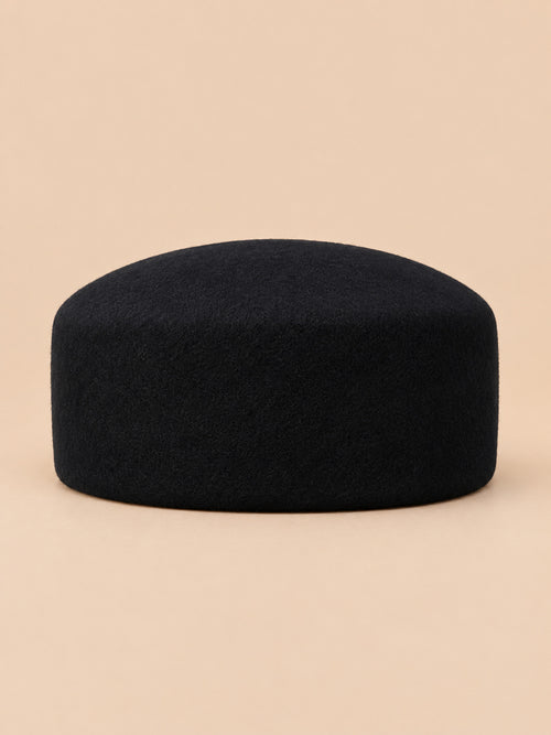 Béret femme en laine feutrée noir, forme dessus plat, vue de face sur fond pêche sable
