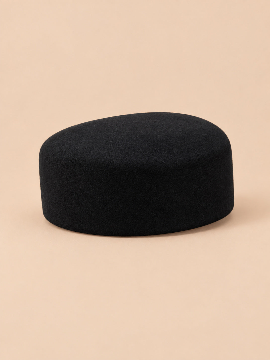 Béret femme en laine feutrée noir, forme dessus plat, vue de trois quarts sur fond pêche sable