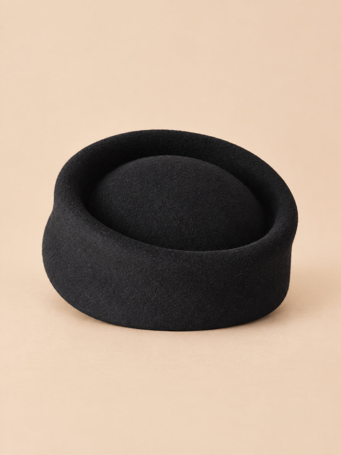 Béret femme en laine feutrée noir, forme pork-pie, vue de face sur fond pêche sable