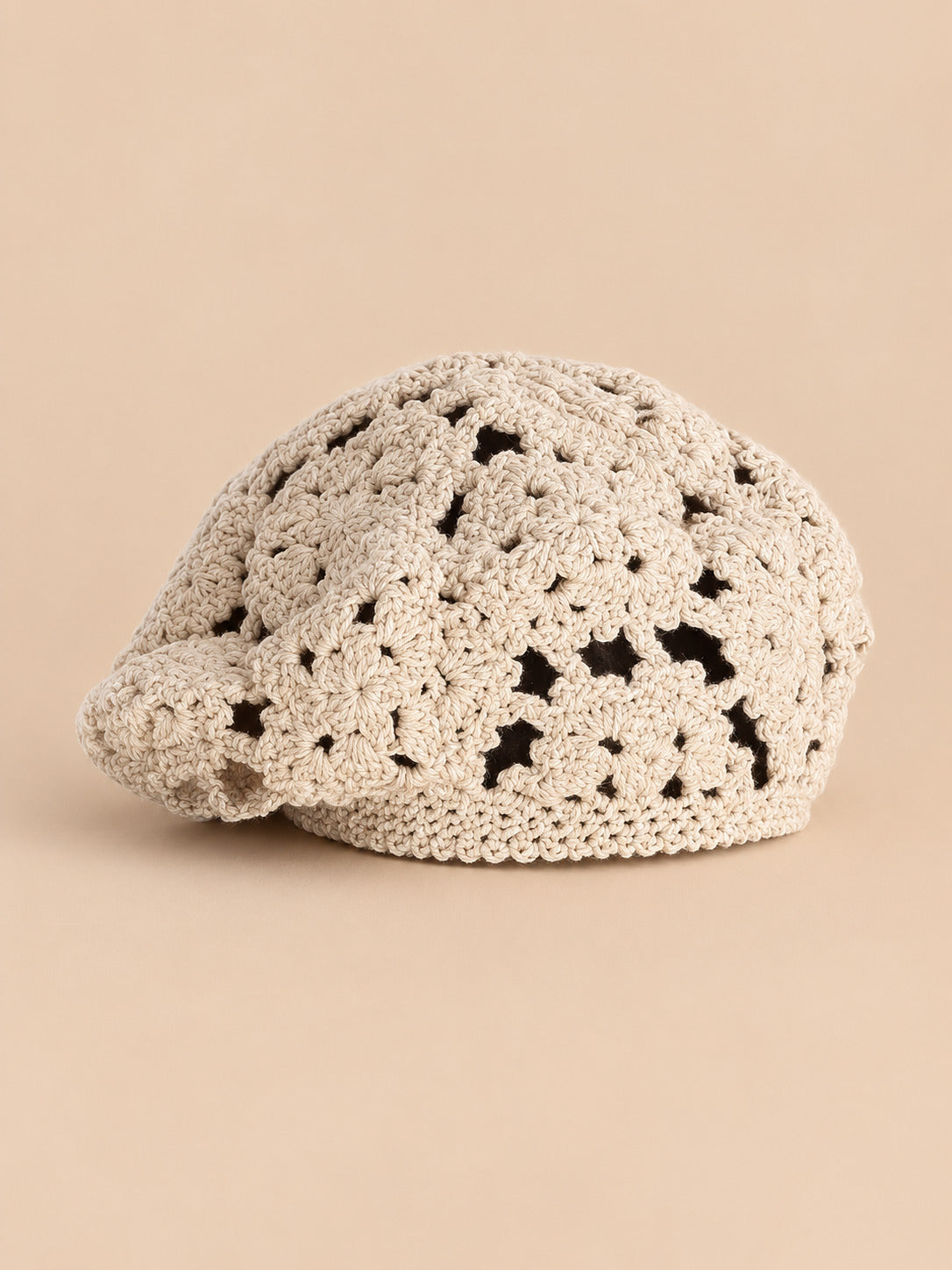 Béret femme beige à fleurs au crochet, vue de trois quarts sur fond pêche sable