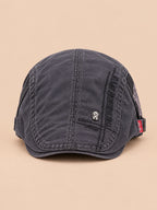 Béret gavroche en coton gris foncé, vue de face sur fond pêche sable