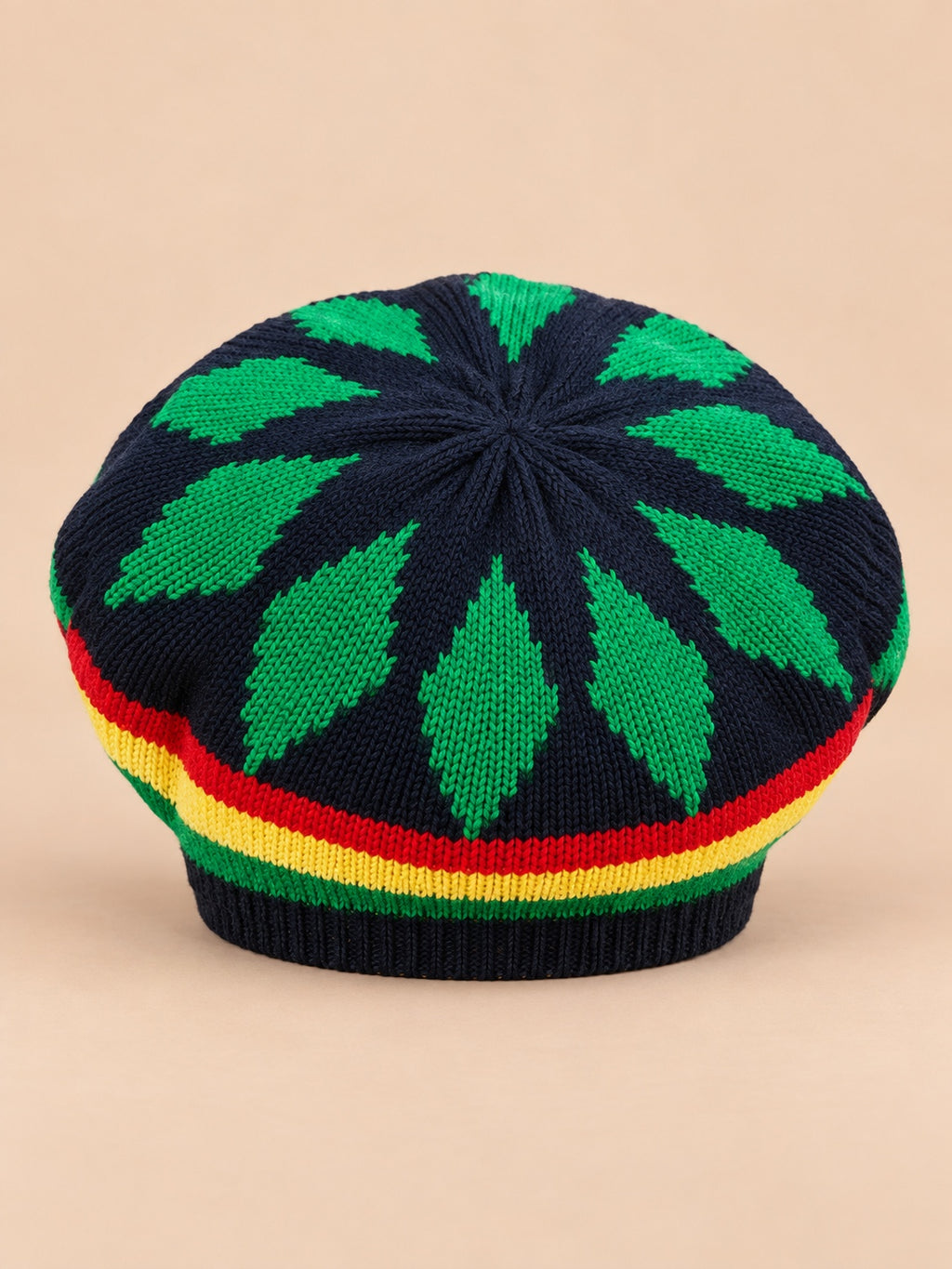 Béret rasta en maille multicolore 1, motifs verts sur fond sombre, vue de face sur fond sable pêche.