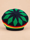 Béret rasta en maille multicolore 1, motifs verts sur fond sombre, vue de face sur fond sable pêche.