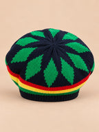 Béret rasta en maille multicolore 1, motifs verts sur fond sombre, vue de face sur fond sable pêche.