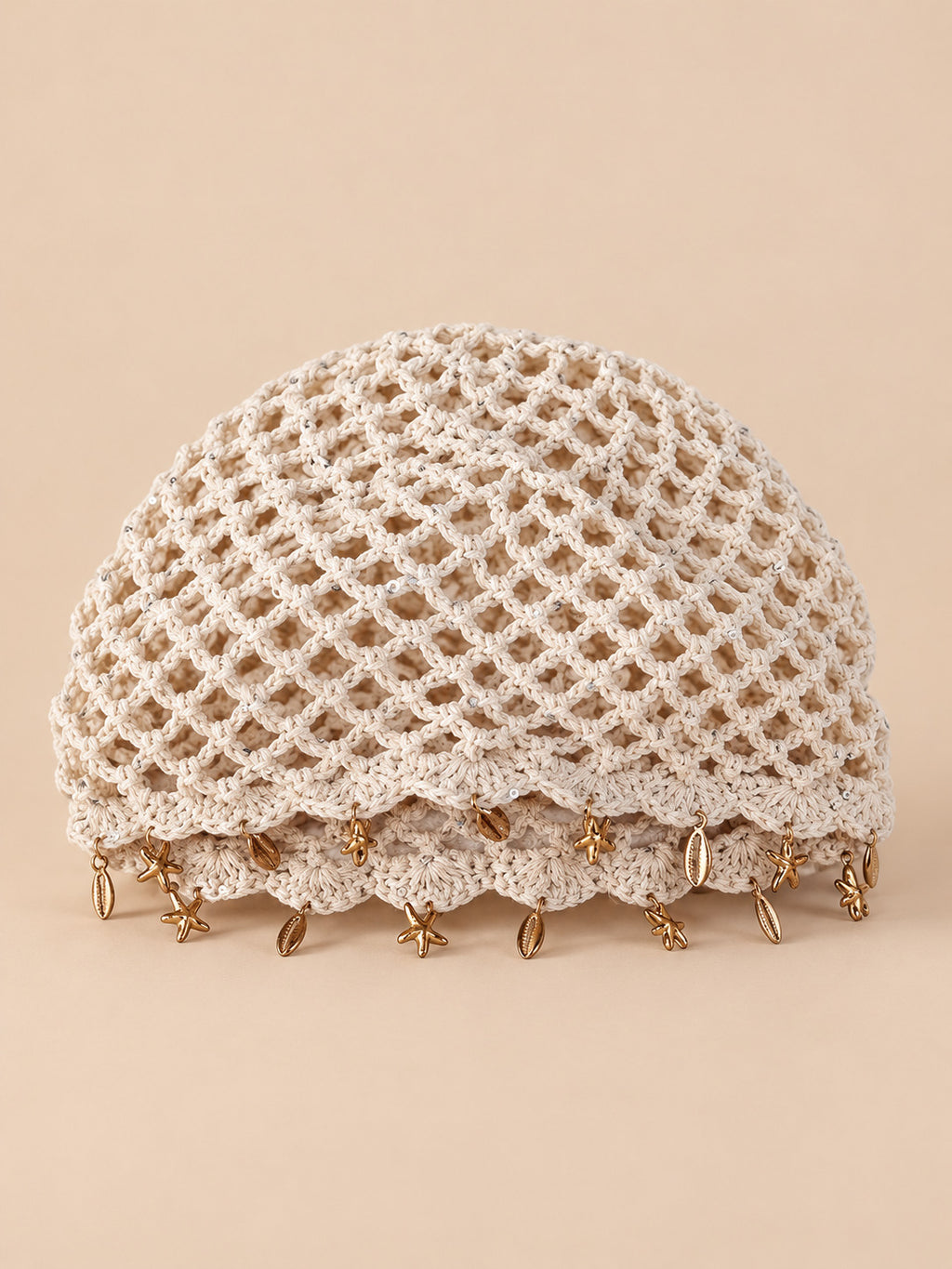 Béret rétro beige ajouré au crochet à franges d'étoiles dorées, vue de face sur fond pêche sable