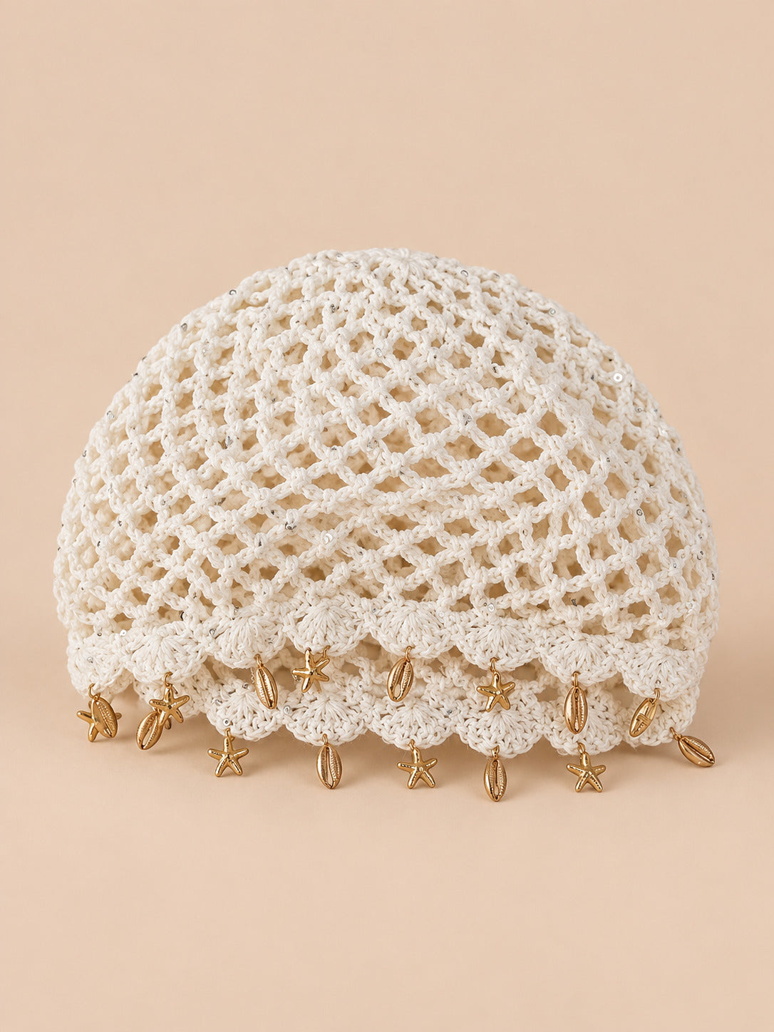 Béret rétro blanc ajouré au crochet à franges d'étoiles dorées, vue de face sur fond pêche sable