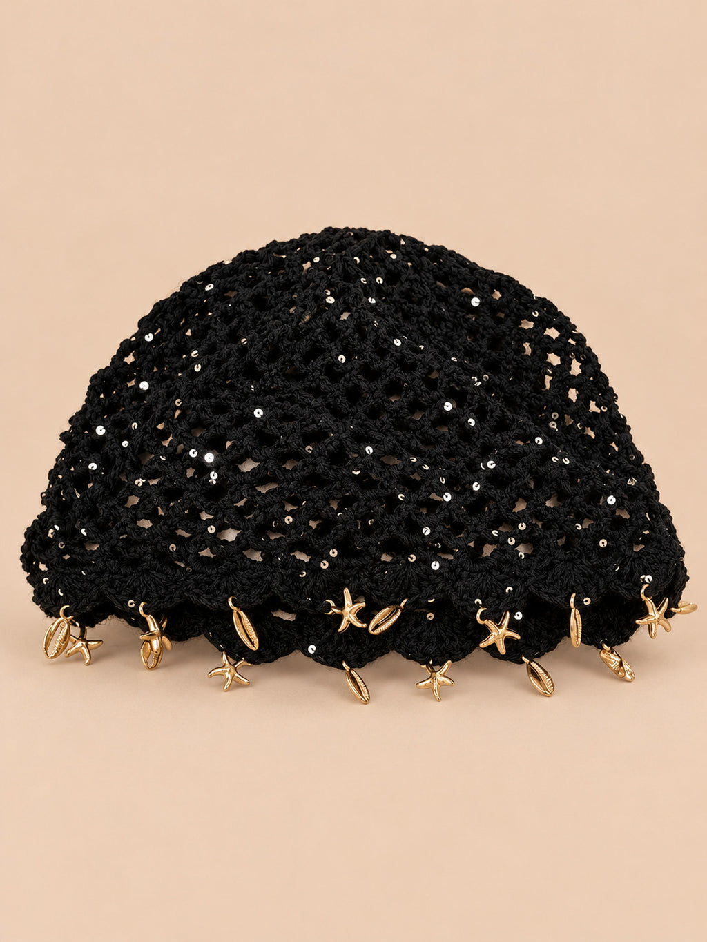 Béret rétro noir ajouré au crochet à franges d'étoiles dorées, vue de face sur fond pêche sable