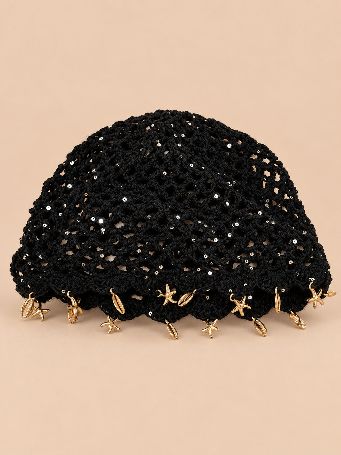 Béret rétro noir ajouré au crochet à franges d'étoiles dorées, vue de face sur fond pêche sable