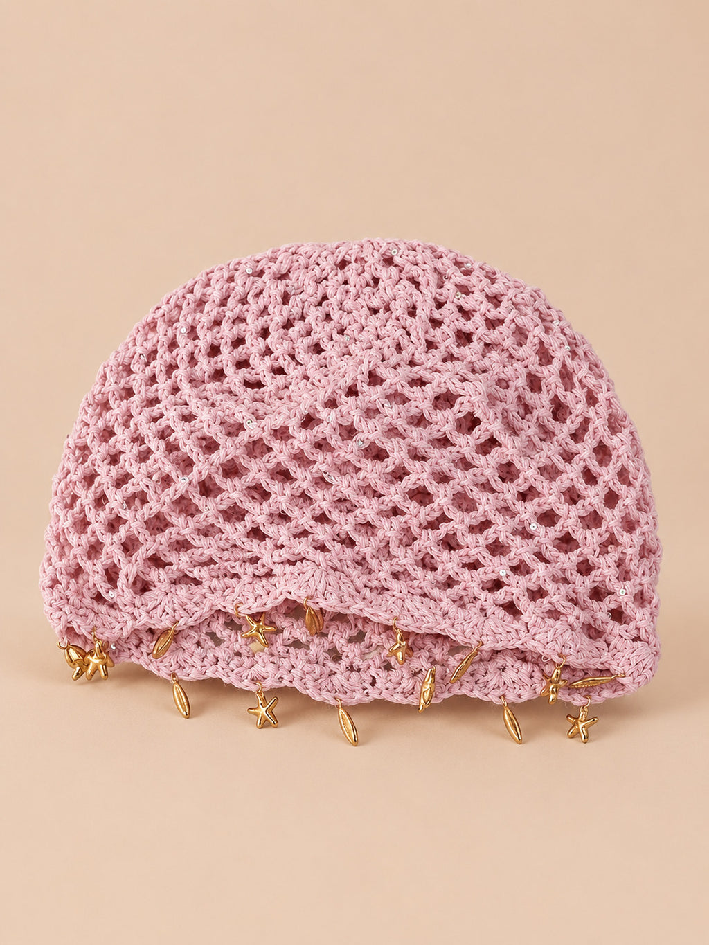 Béret rétro rose ajouré au crochet à franges d'étoiles dorées, vue de face sur fond pêche sable