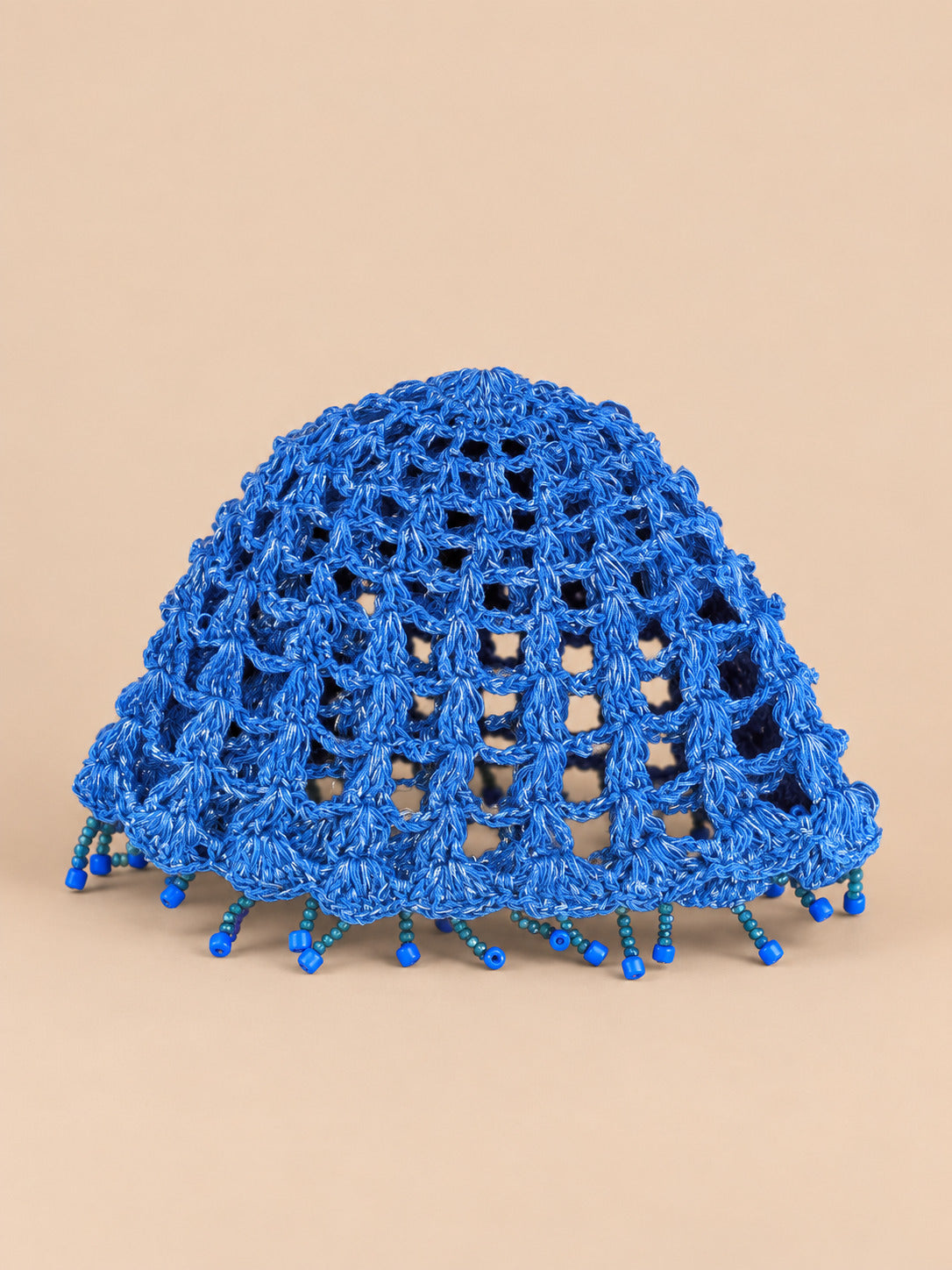 Béret crochet rétro bleu ajouré à franges de perles, vue de face sur fond pêche sable