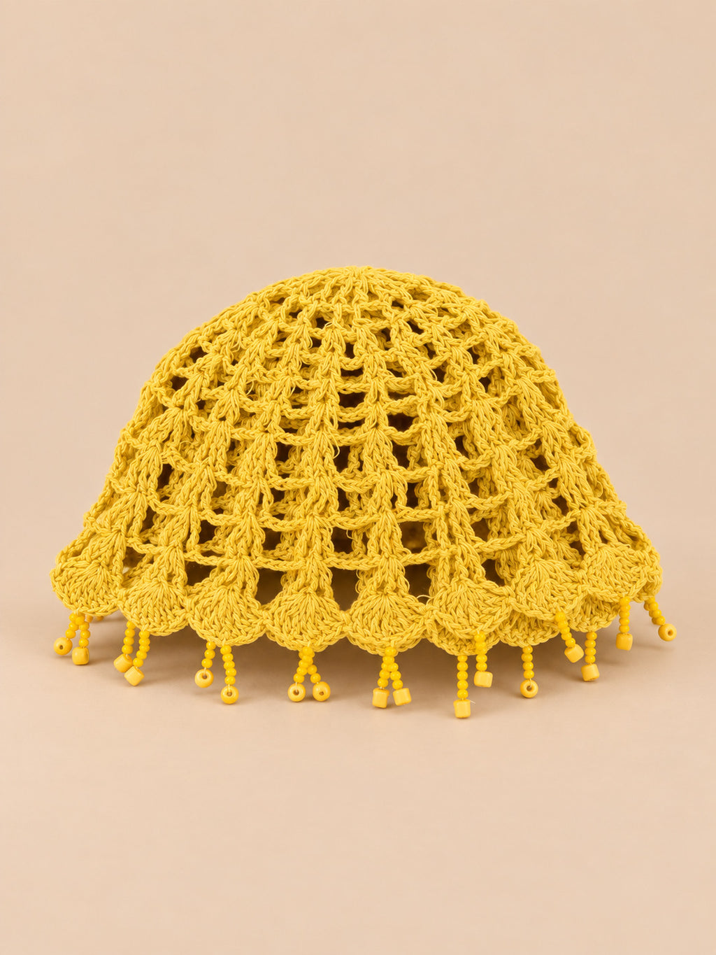 Béret crochet rétro jaune ajouré à franges de perles, vue de face sur fond pêche sable