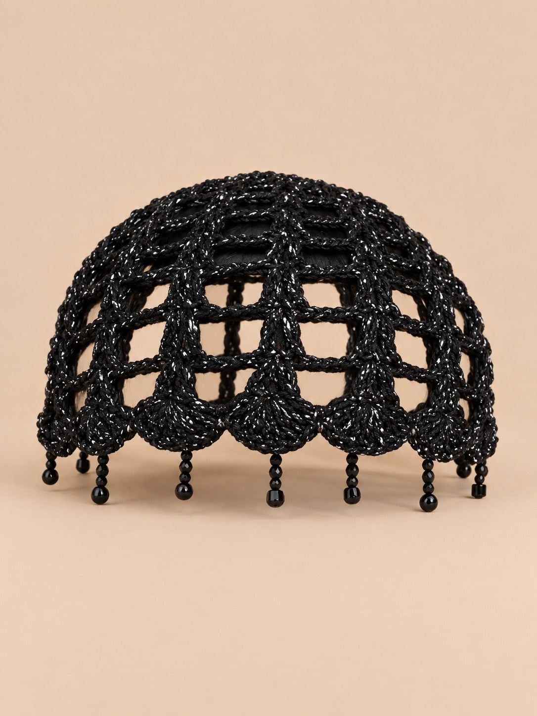 Béret crochet rétro noir ajouré à franges de perles, vue de face sur fond pêche sable