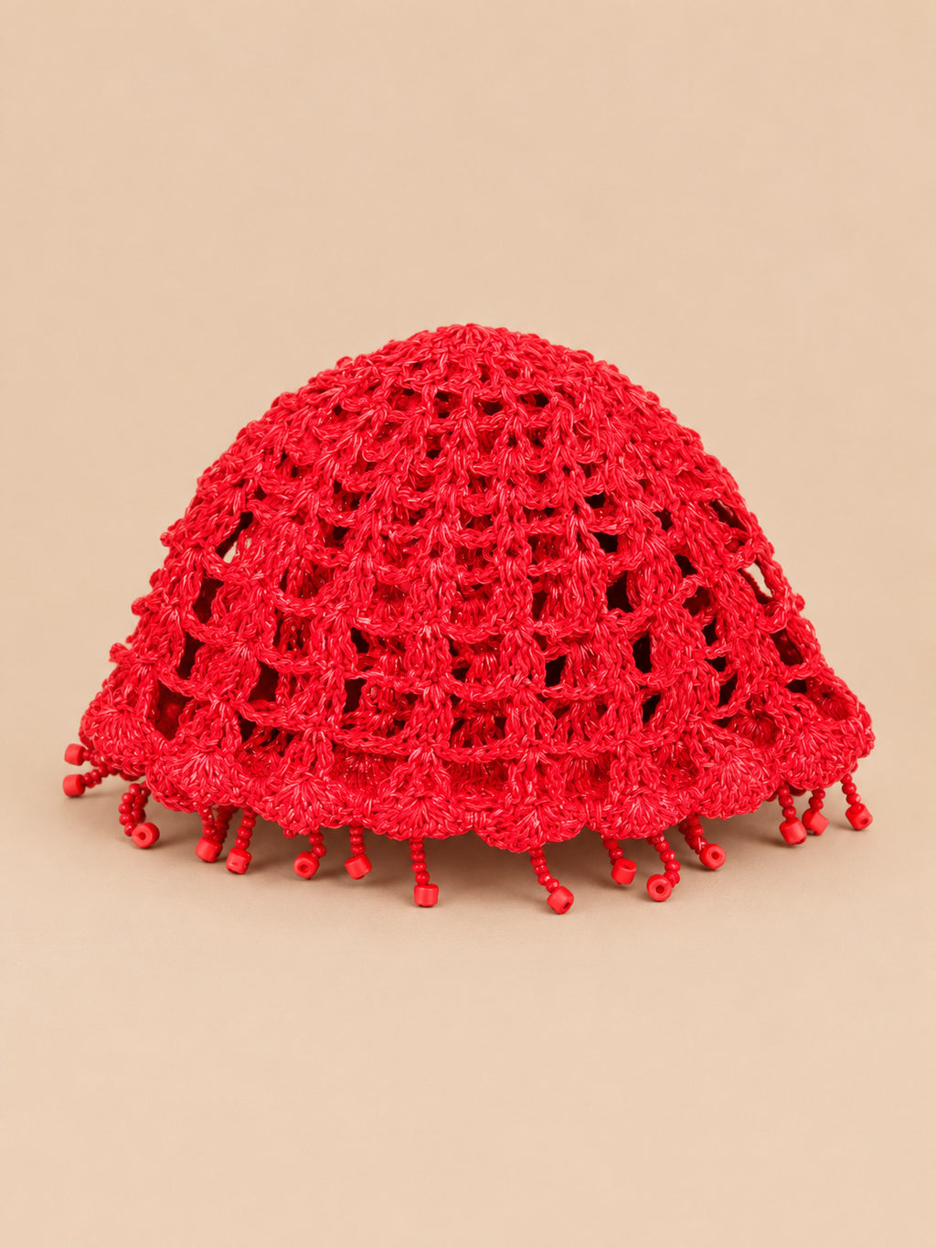 Béret crochet rétro rouge ajouré à franges de perles, vue de face sur fond pêche sable