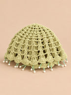 Béret crochet rétro vert ajouré à franges de perles, vue de face sur fond pêche sable