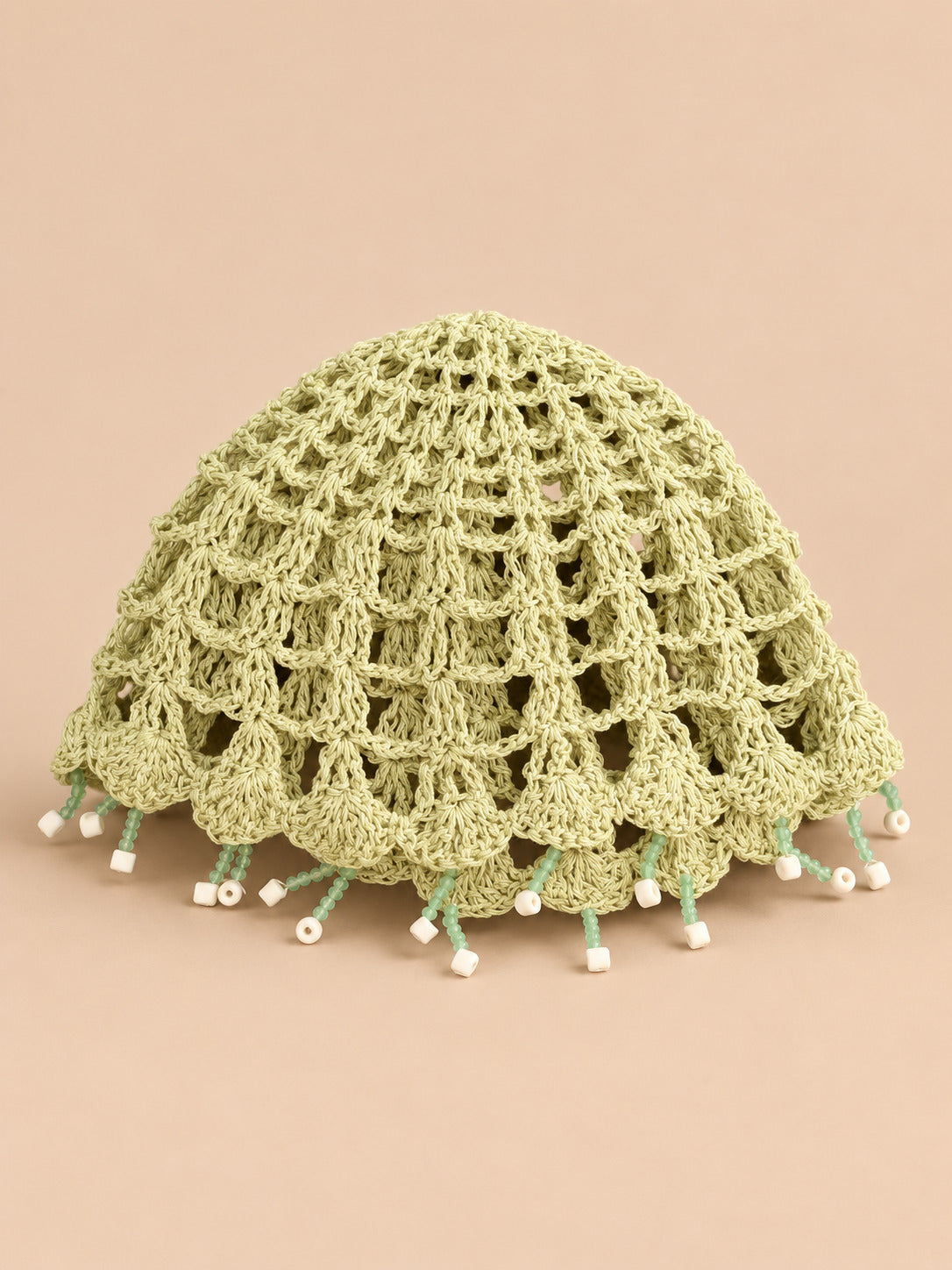 Béret crochet rétro vert ajouré à franges de perles, vue de face sur fond pêche sable