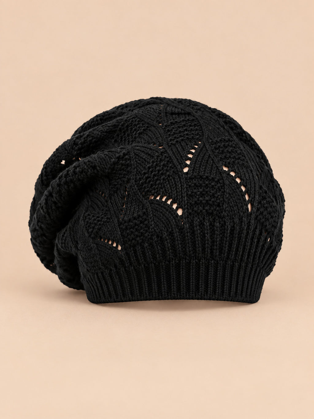 Bonnet béret torsadé ample noir, vue de face sur fond pêche sable