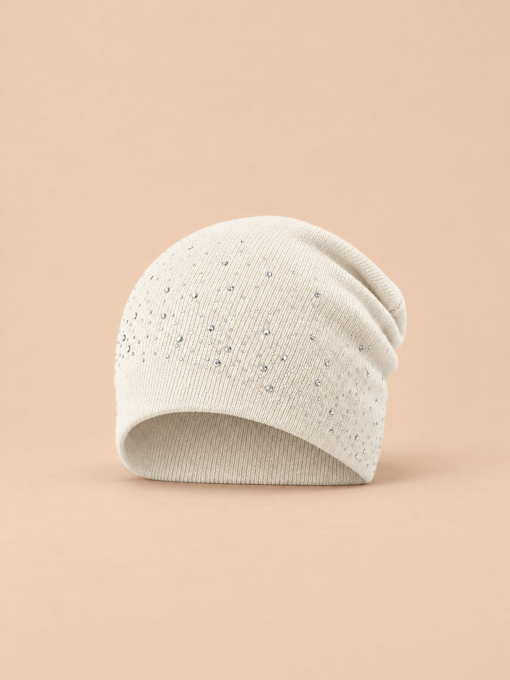 Bonnet femme tricoté à strass blanc, vue de face sur fond pêche sable