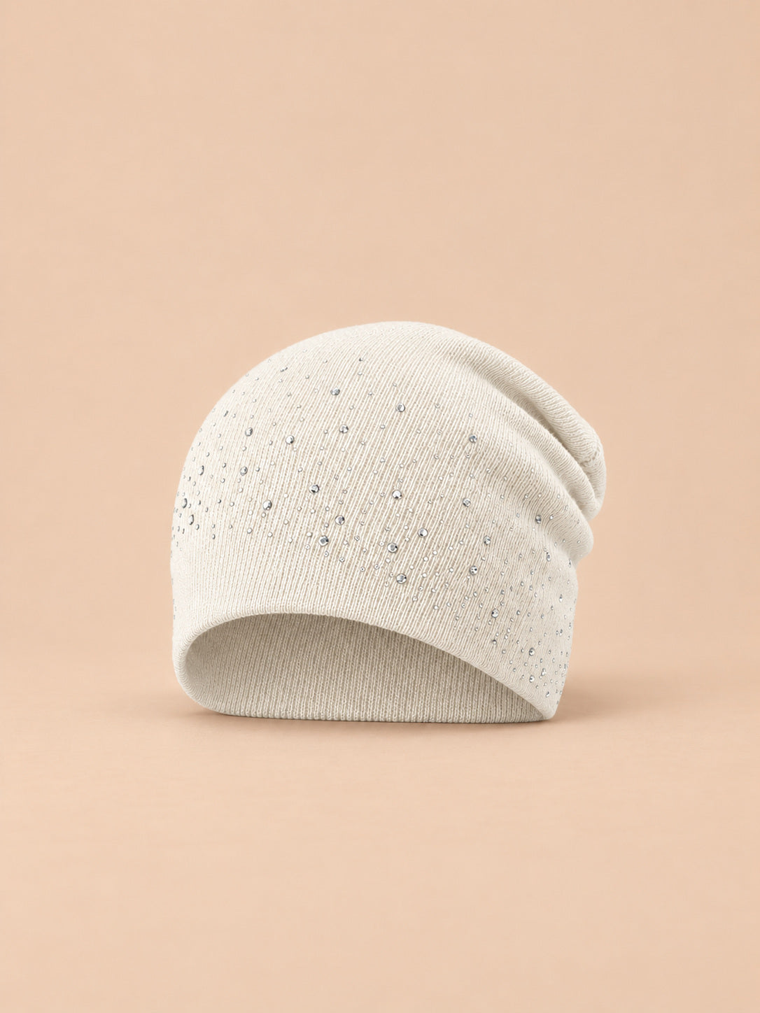 Bonnet femme tricoté à strass blanc, vue de face sur fond pêche sable
