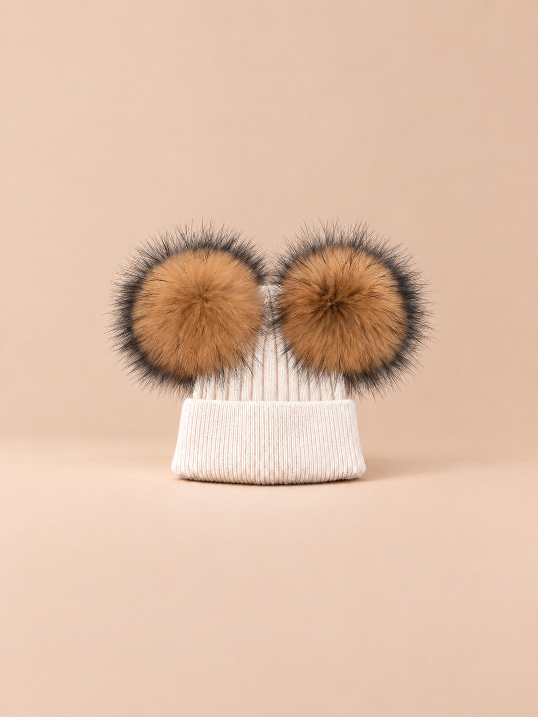 Bonnet double pompon, beige, pompons naturels, vue de face sur fond pêche sable.