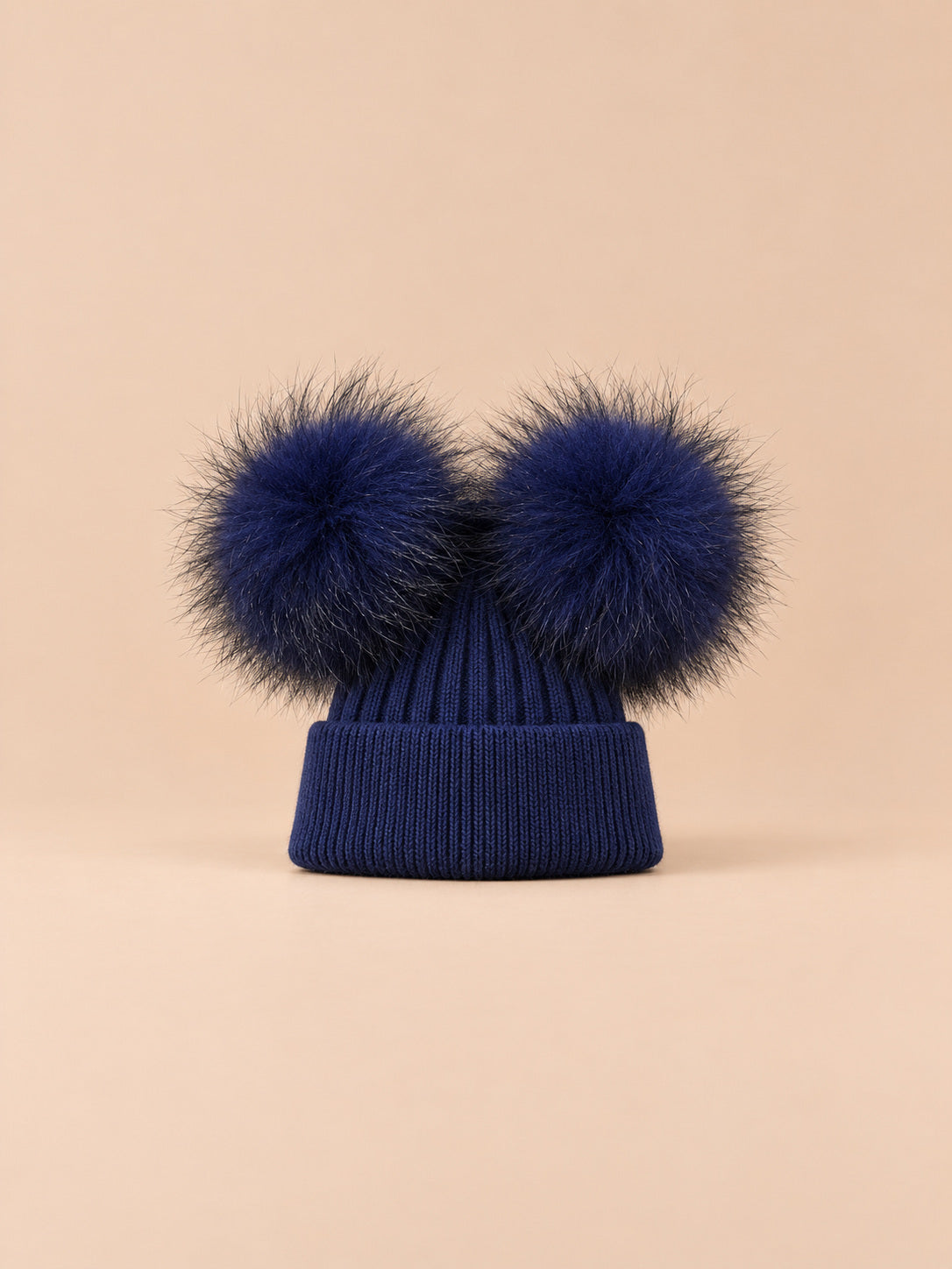 Bonnet double pompon, bleu marine, pompons assortis, vue de face sur fond pêche sable.