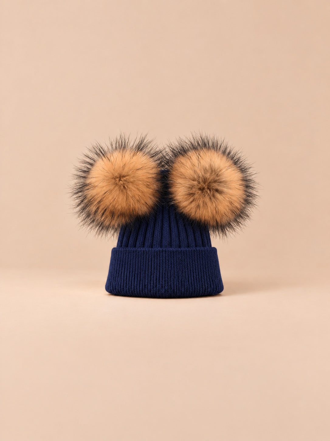 Bonnet double pompon, bleu marine, pompons naturels, vue de face sur fond pêche sable.