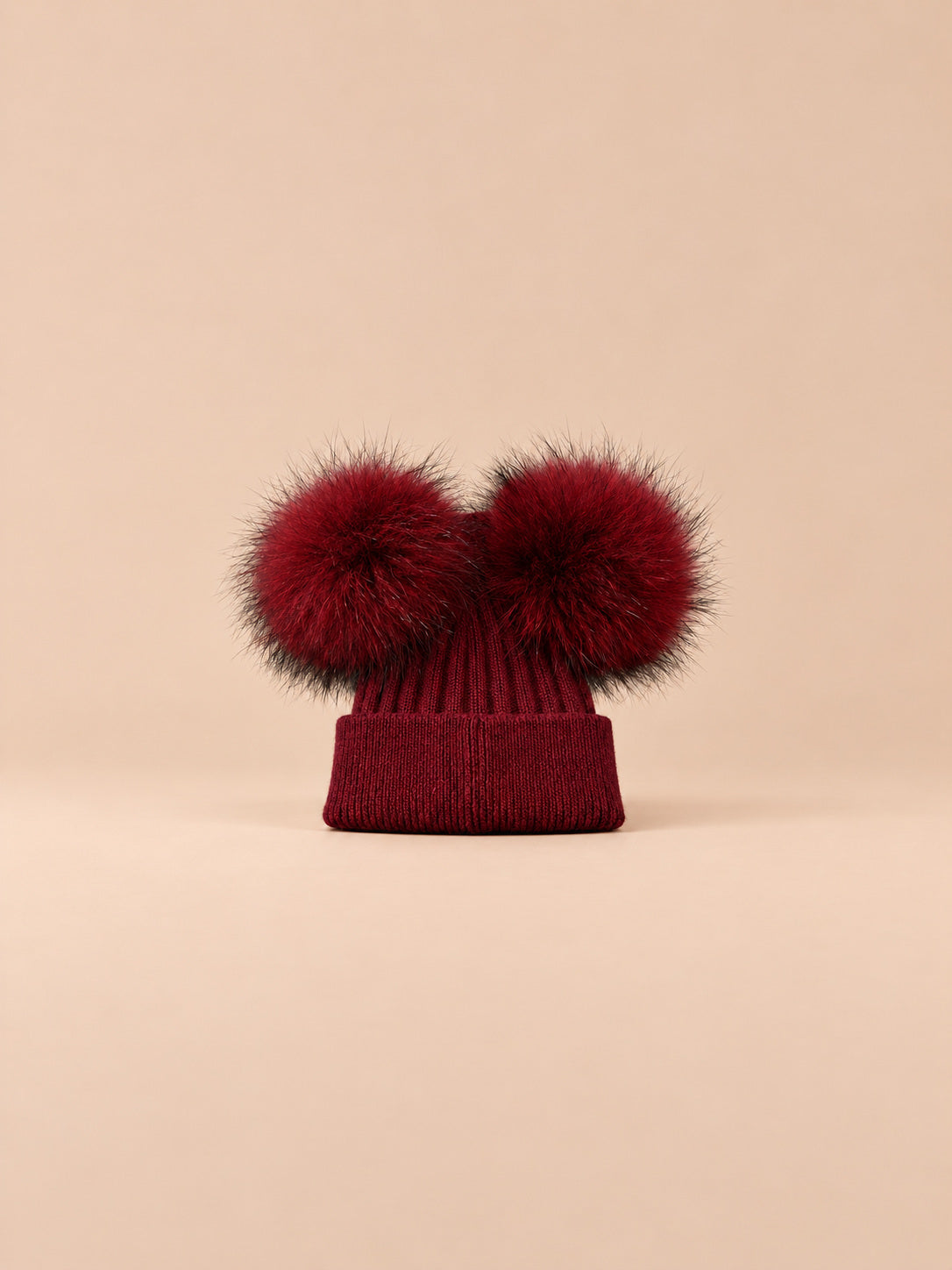 Bonnet double pompon, bordeaux, pompons assortis, vue de face sur fond pêche sable.