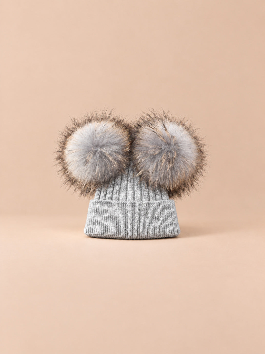 Bonnet double pompon, gris clair, pompons assortis, vue de face sur fond pêche sable.