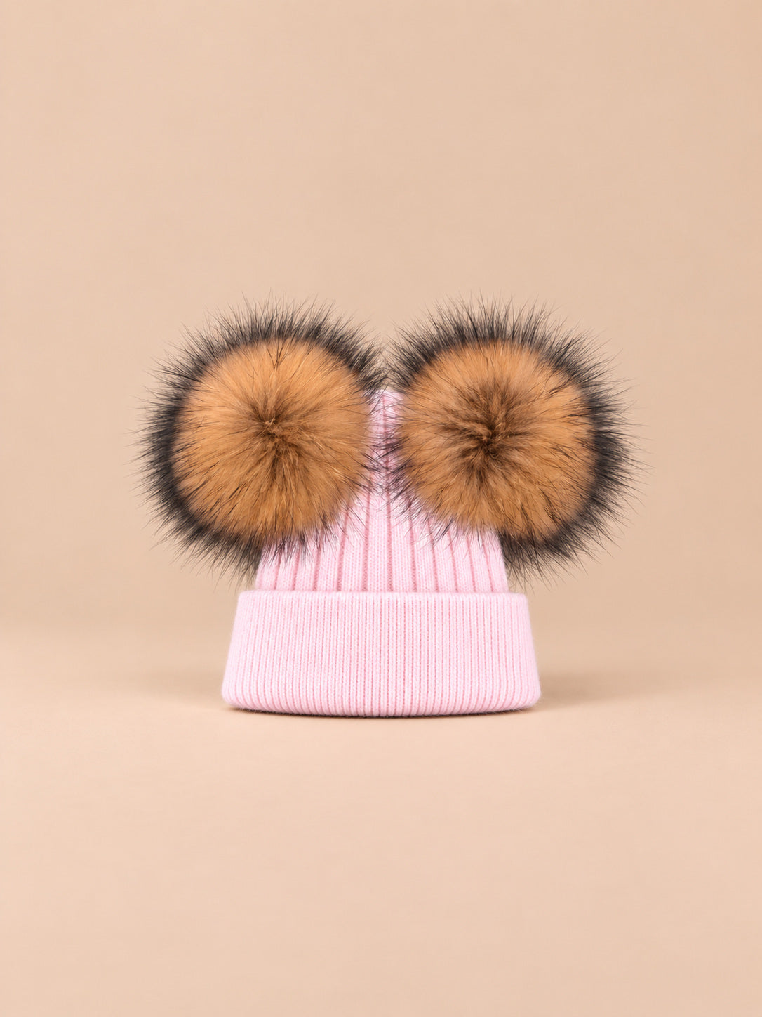 Bonnet double pompon, rose pâle, pompons naturels, vue de face sur fond pêche sable.