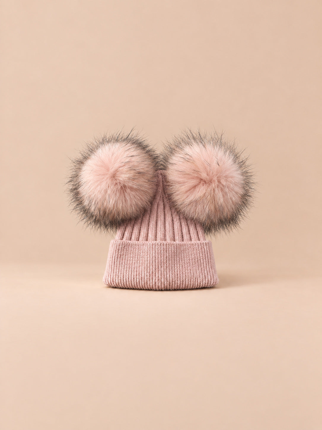 Bonnet double pompon, rose poudré, pompons assortis, vue de face sur fond pêche sable.
