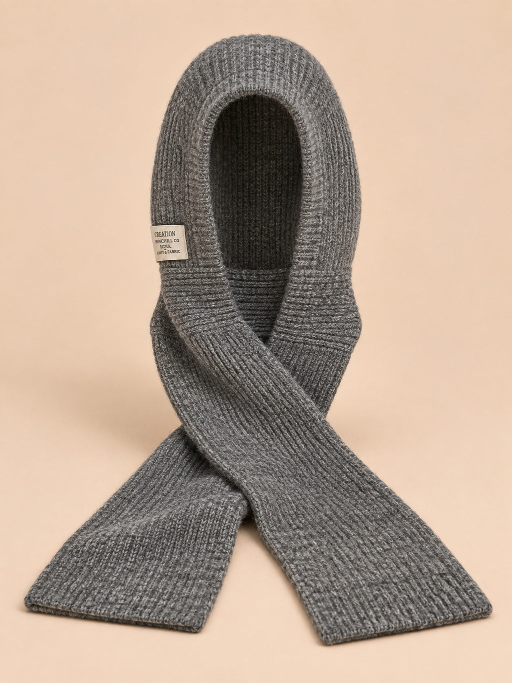Cagoule bonnet-écharpe gris en maille, vue de face sur fond pêche sable