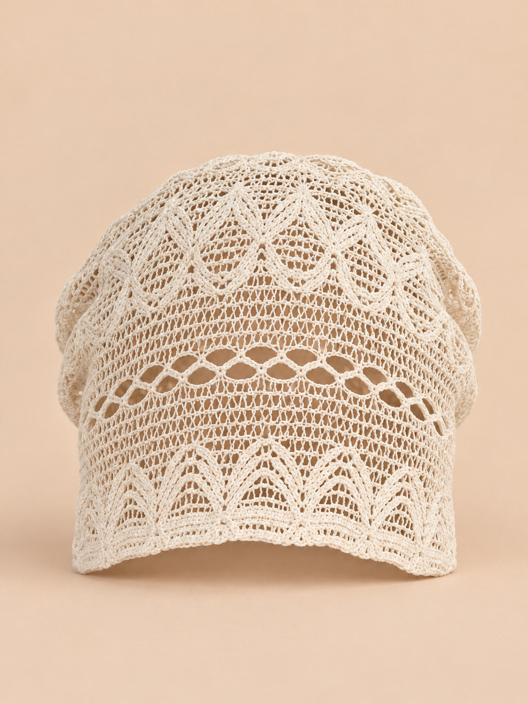 Bonnet calotte froncée beige en dentelle crochet ajourée, vue de face sur fond pêche sable