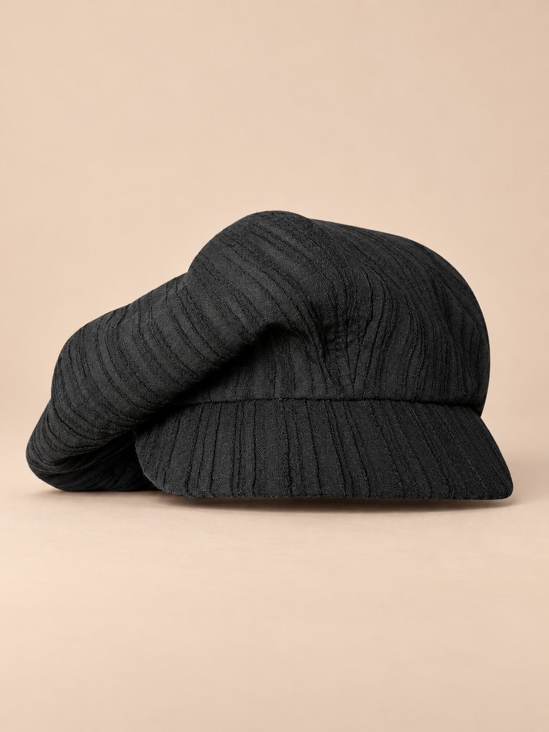 Casquette gavroche vintage noir, vue de face sur fond pêche sable