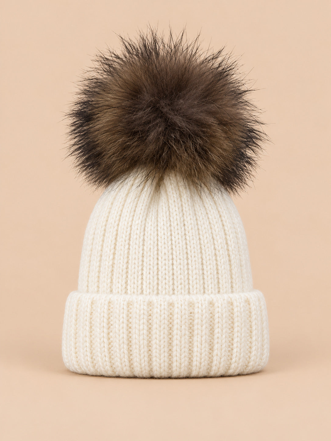 Bonnet enfant à pompon blanc, vue de face sur fond pêche sable