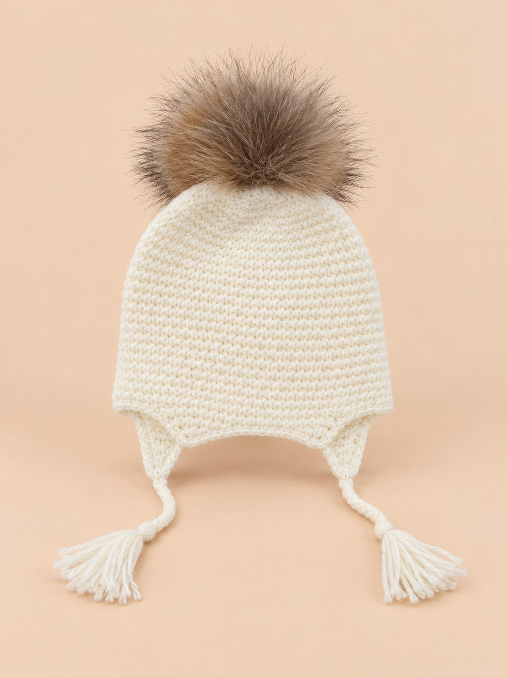Bonnet enfant à pompon blanc torsade, vue de face sur fond pêche sable
