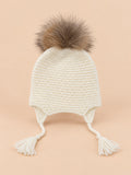 Bonnet enfant à pompon blanc torsade, vue de face sur fond pêche sable
