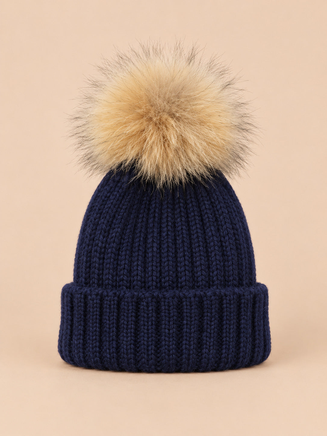 Bonnet enfant à pompon bleu fonce, vue de face sur fond pêche sable