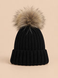 Bonnet enfant à pompon noir, vue de face sur fond pêche sable