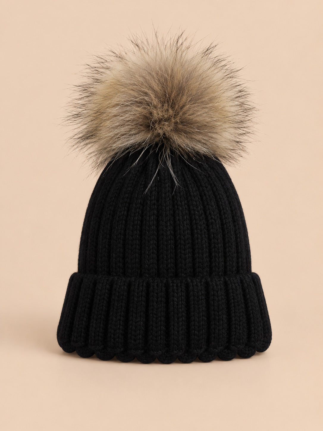 Bonnet enfant à pompon noir, vue de face sur fond pêche sable