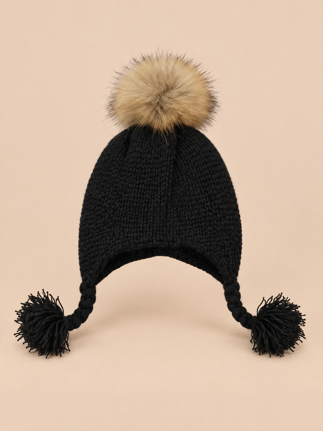 Bonnet enfant à pompon noir torsade, vue de face sur fond pêche sable