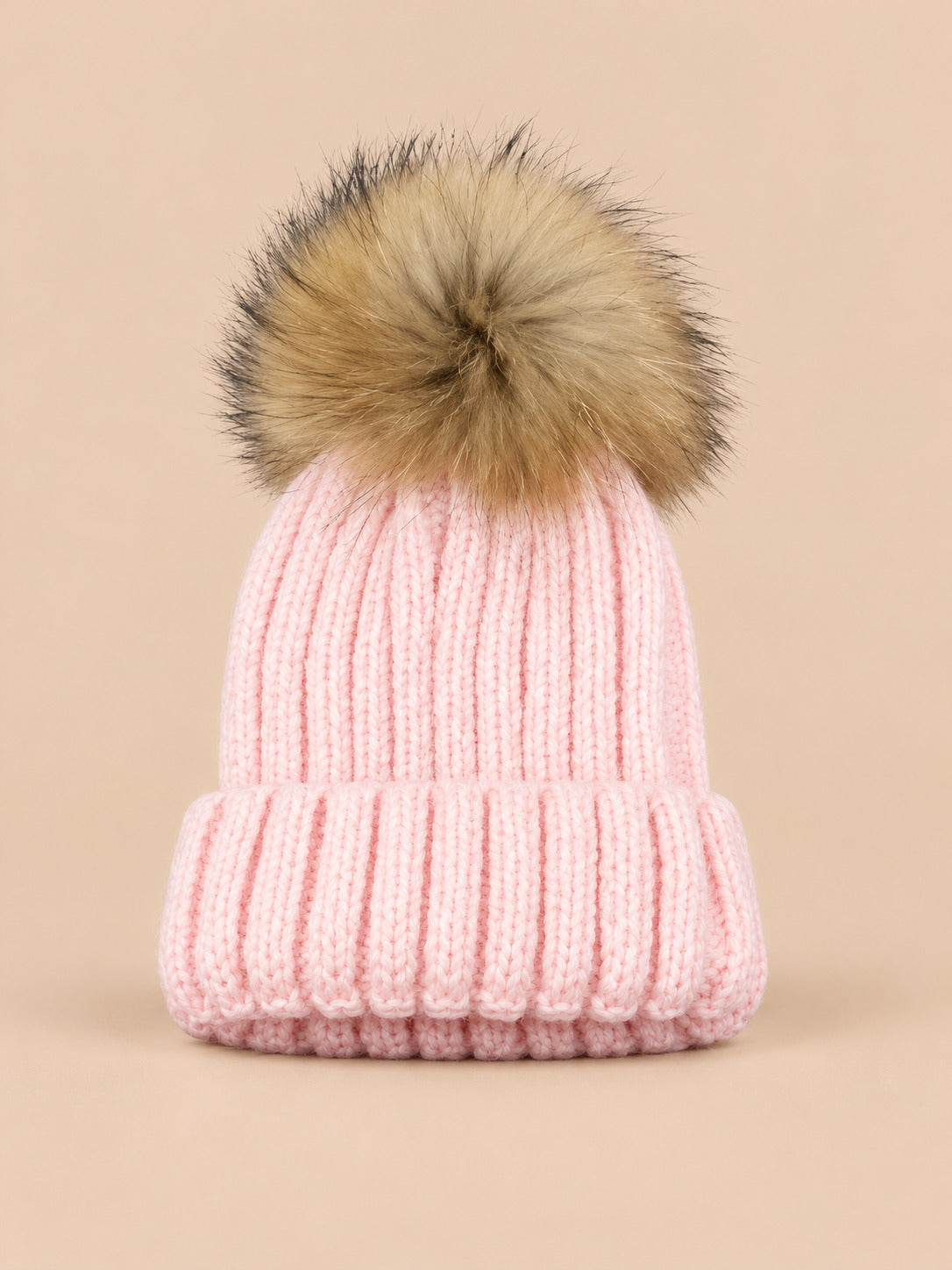 Bonnet enfant à pompon rose, vue de face sur fond pêche sable