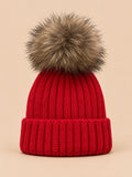 Bonnet enfant à pompon rouge, vue de face sur fond pêche sable