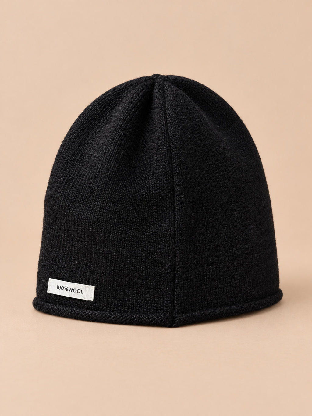 Bonnet femme en pure laine noir, vue de trois quarts, fond pêche sable