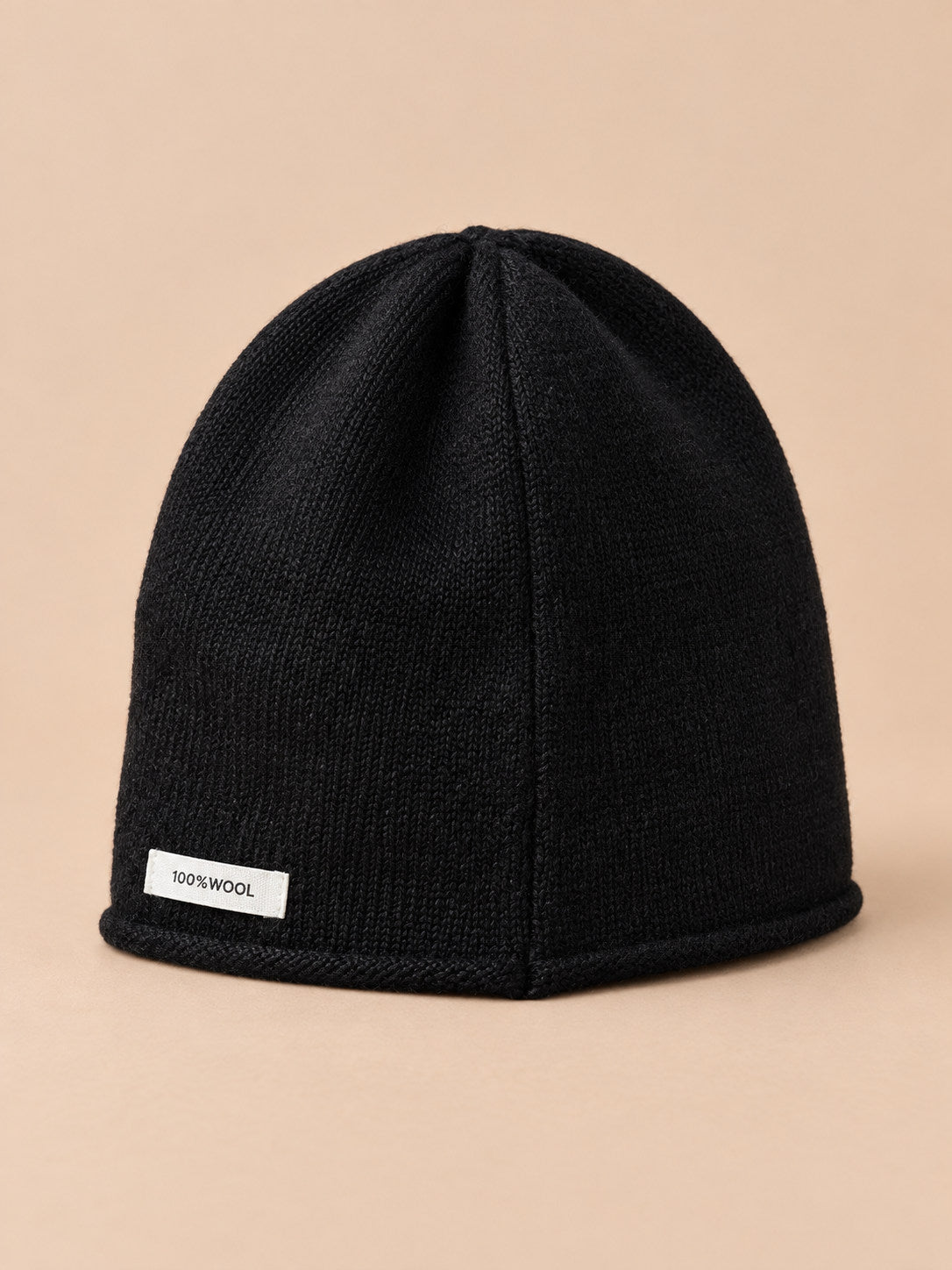 Bonnet femme en pure laine noir, vue de trois quarts, fond pêche sable