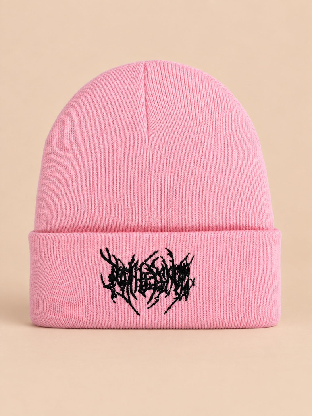 Bonnet en maille chaud rose à broderie noire, vue de face sur fond pêche sable